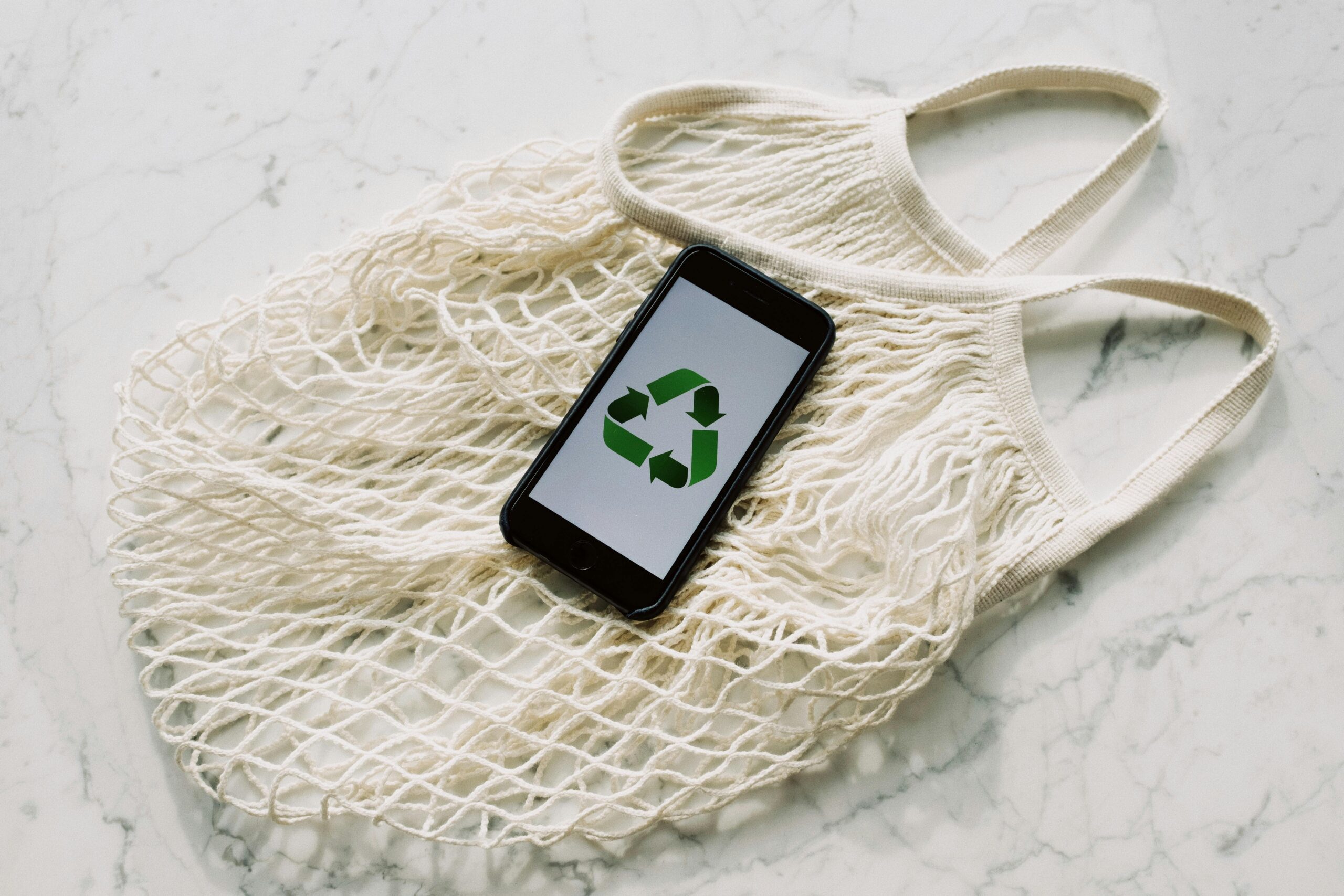 A mobile phone with the recyclability logo on a white cloth bag